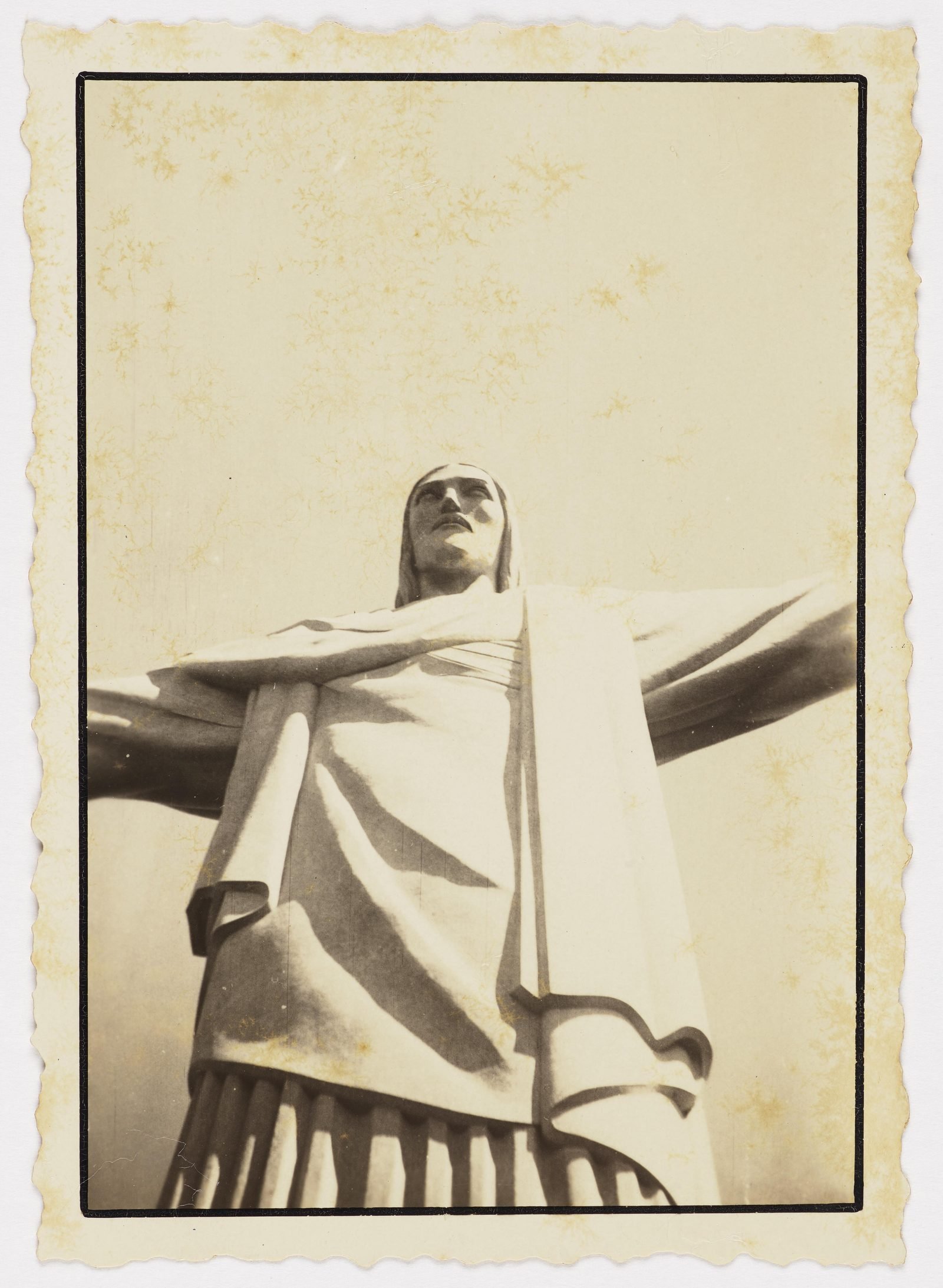 Fotografia antiga do Cristo Redentor visto de baixo, de braços abertos