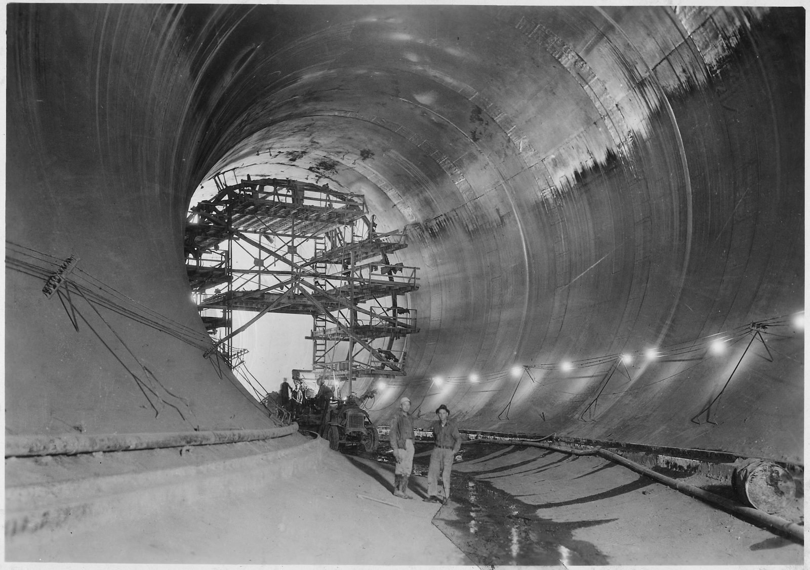Interior de un túnel de desvío ya revestido de concreto, con un andamio metálico y dos hombres en el piso