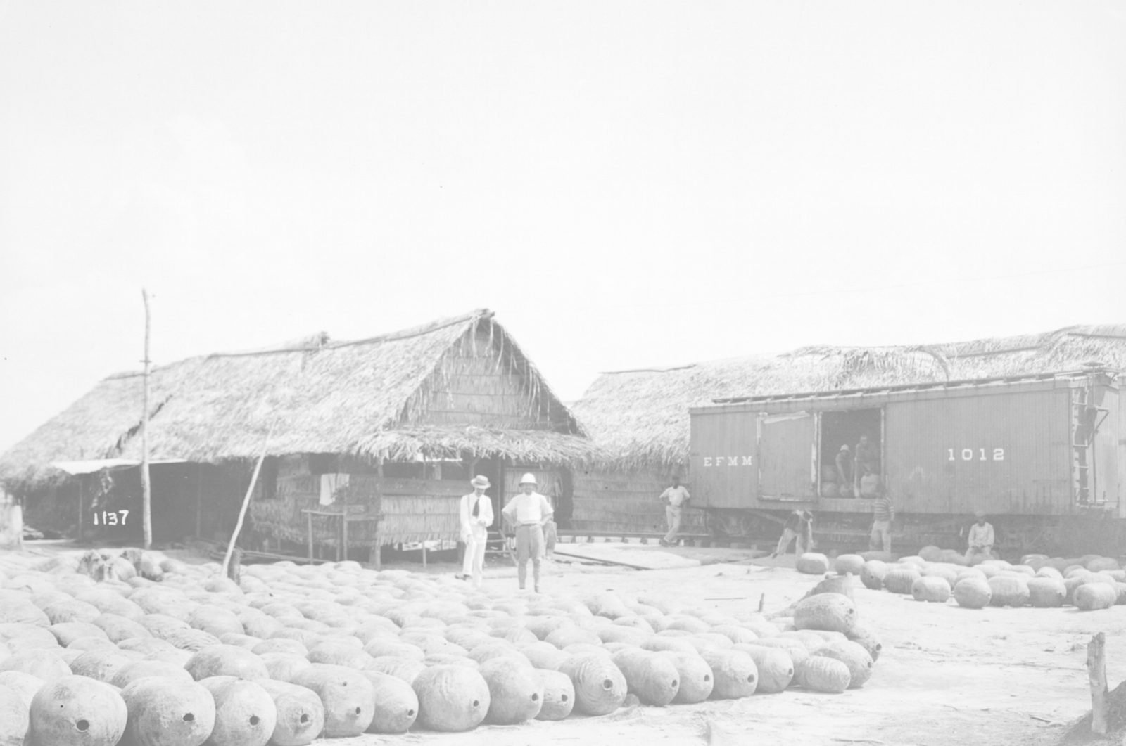 Hundreds of rubber balls lined up on the ground in front of thatched sheds and a freight car marked EFMM