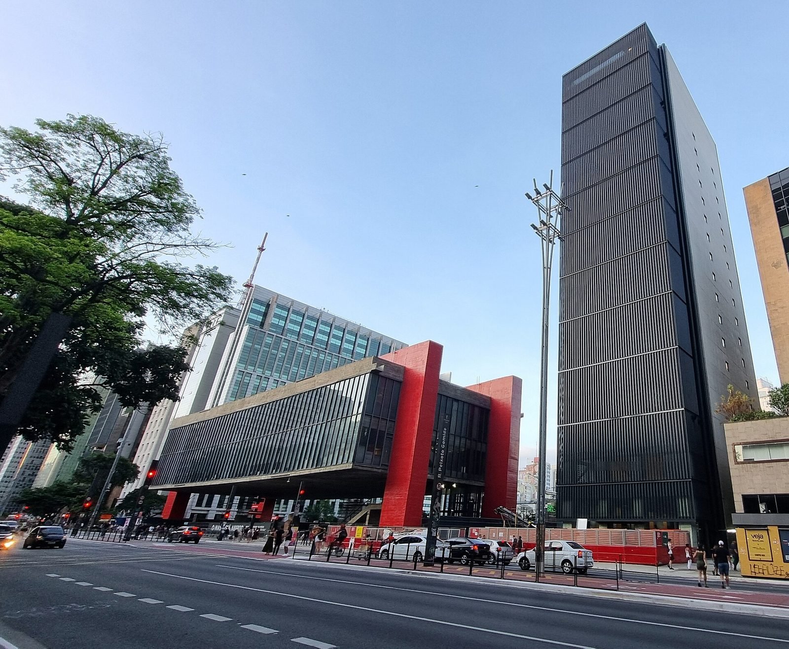 A caixa de vidro com pórticos vermelhos do MASP, baixa e comprida, ao lado de uma torre estreita e escura de muitos andares, numa avenida sob céu azul