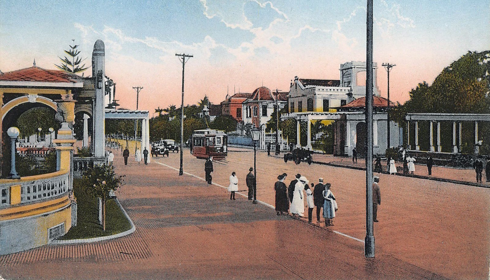 Cartão-postal colorido antigo: uma avenida larga com bonde e pedestres de roupas dos anos 1920, um pavilhão amarelo com telhado vermelho à esquerda e uma pérgola de colunas à direita