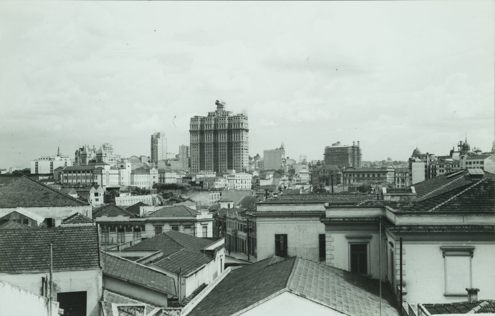Old black-and-white photograph: low rooftops of downtown São Paulo in the foreground and, behind them, a single building much taller than all the others