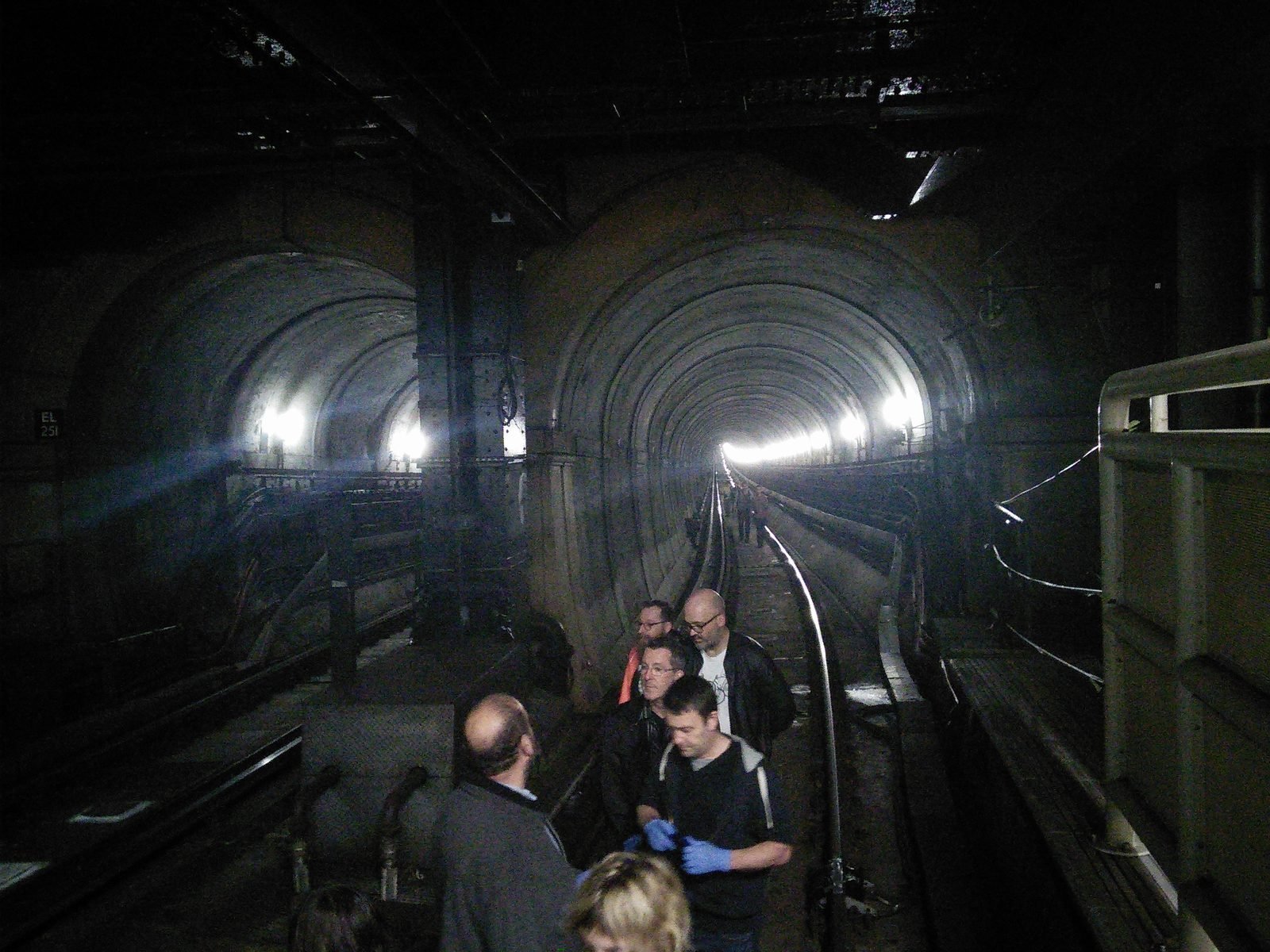 People walking on the tracks at the dark entrance of two tunnel galleries side by side, lit in the distance