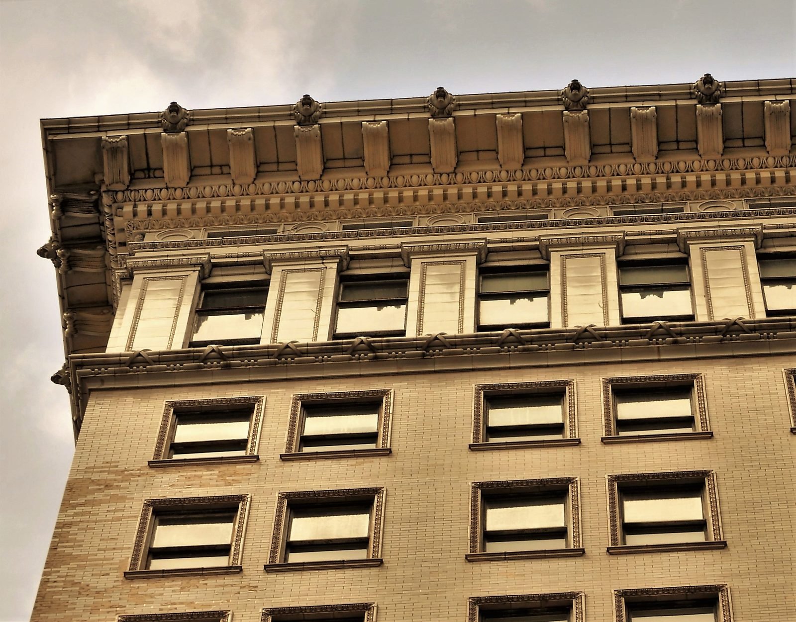 Detail of the top of a building: a decorated projecting cornice, a top floor with pilasters and windows and, below, rows of windows in a light brick wall