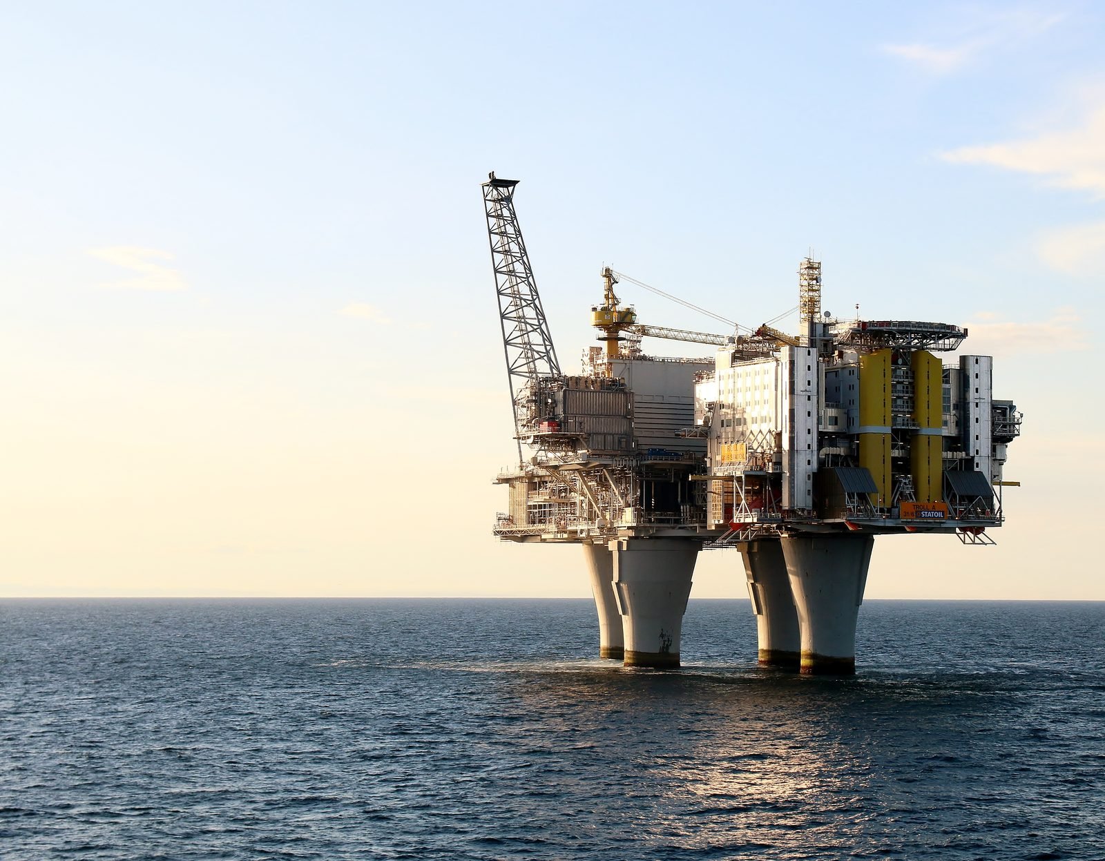 Las columnas de concreto de la plataforma saliendo del agua, con la cubierta de módulos blancos y amarillos y una grúa de celosía en lo alto