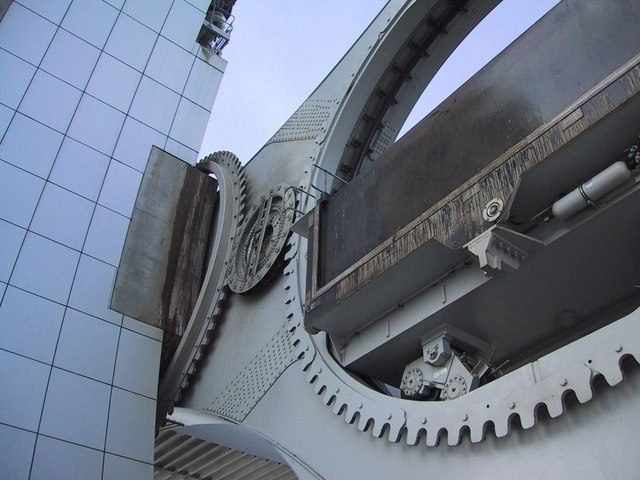 Detalle de cerca de grandes engranajes de acero con dientes alrededor de un anillo, junto al extremo de una góndola y a una pared de paneles