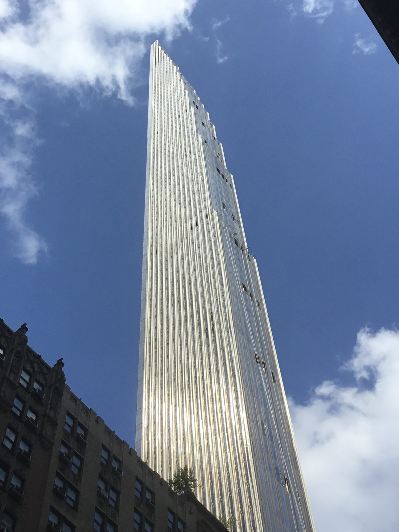 Pale facade seen from below, covered in narrow, repeated vertical piers rising until they stand out against the blue sky
